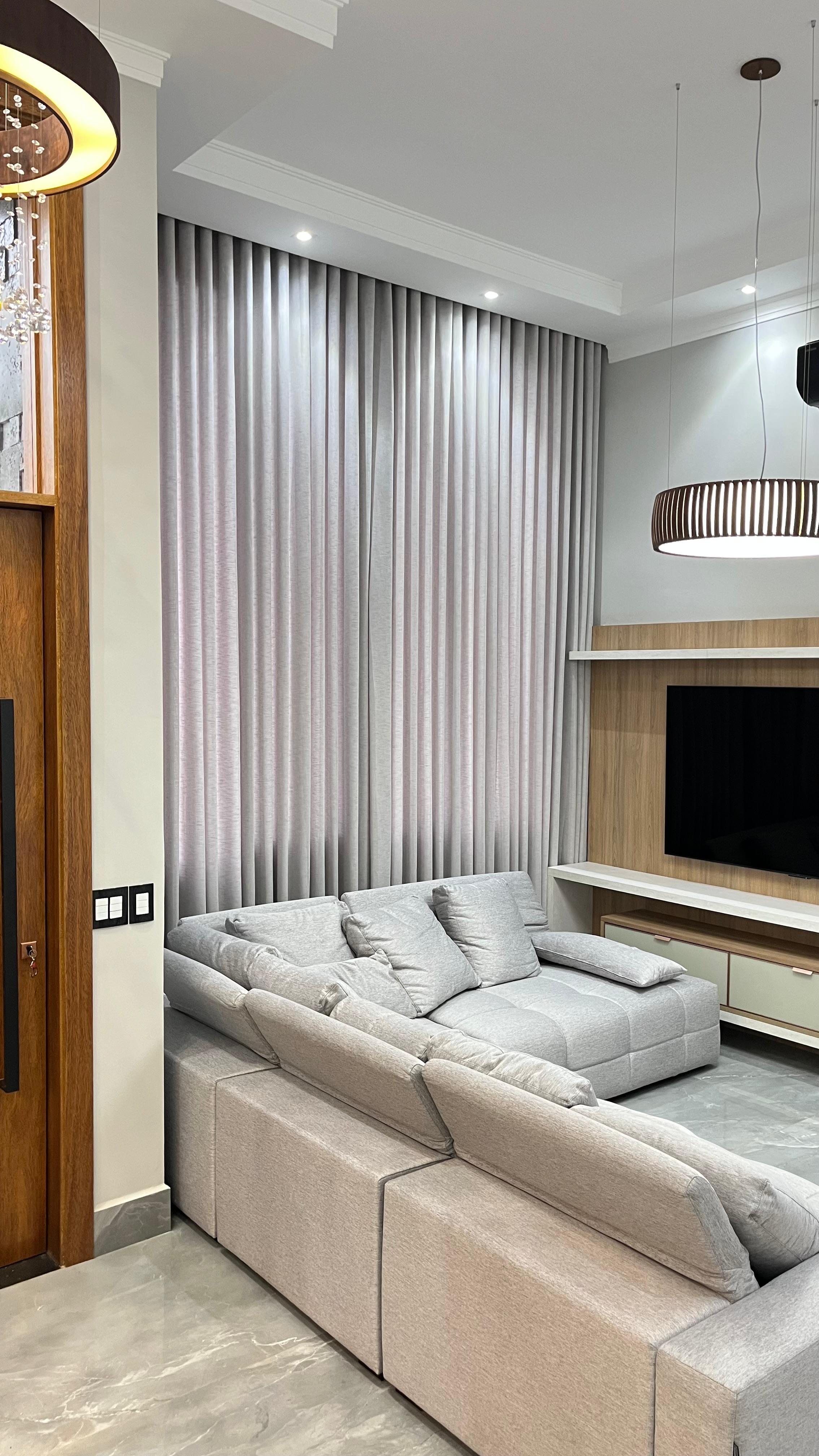 Cortina de voil em sala de estar com sofá amplo e painel de TV