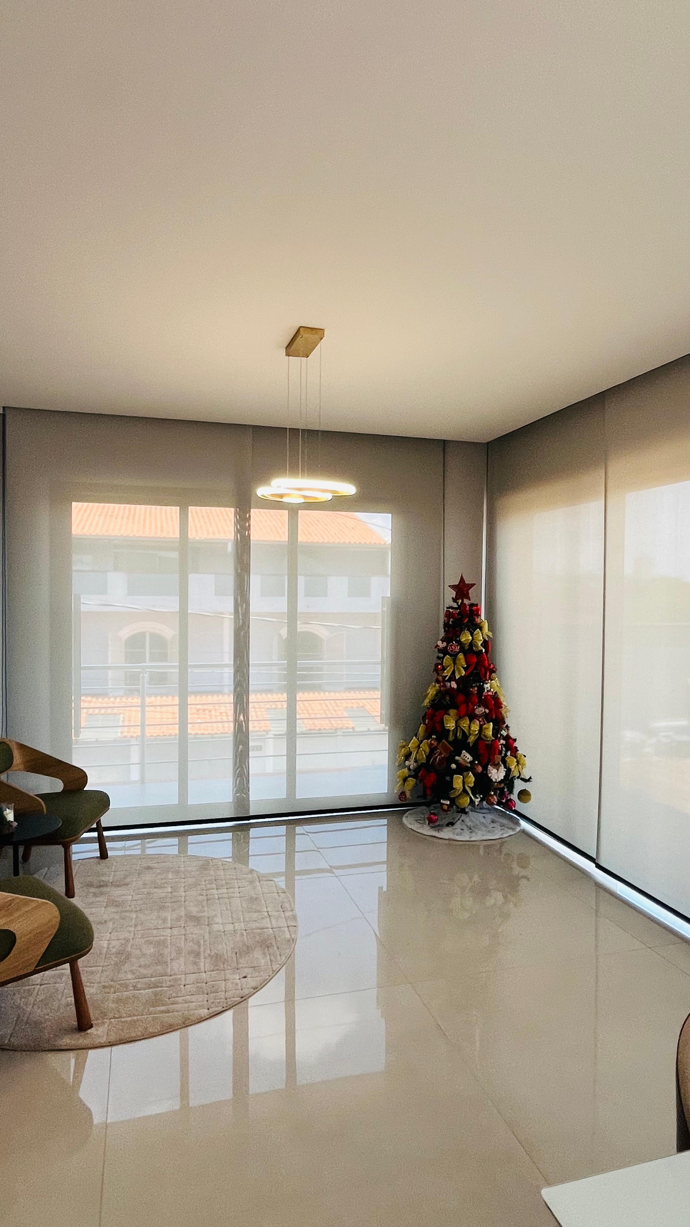 Sala de estar de pé direito alto com cortina de voil, poltronas verdes e mesa de jantar